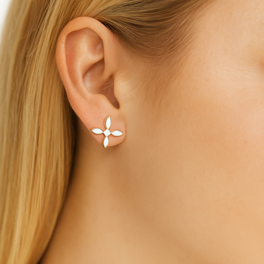 Close-up of a woman's ear wearing a gold and white cross-shaped earring with a blurred background