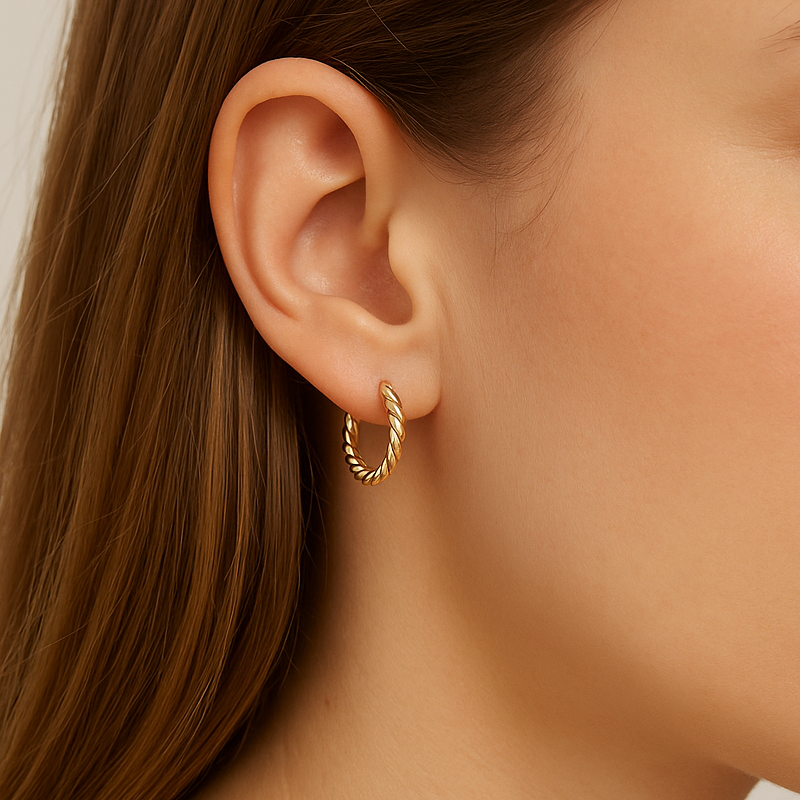Close-up of a person wearing a gold hoop earring with a neutral background