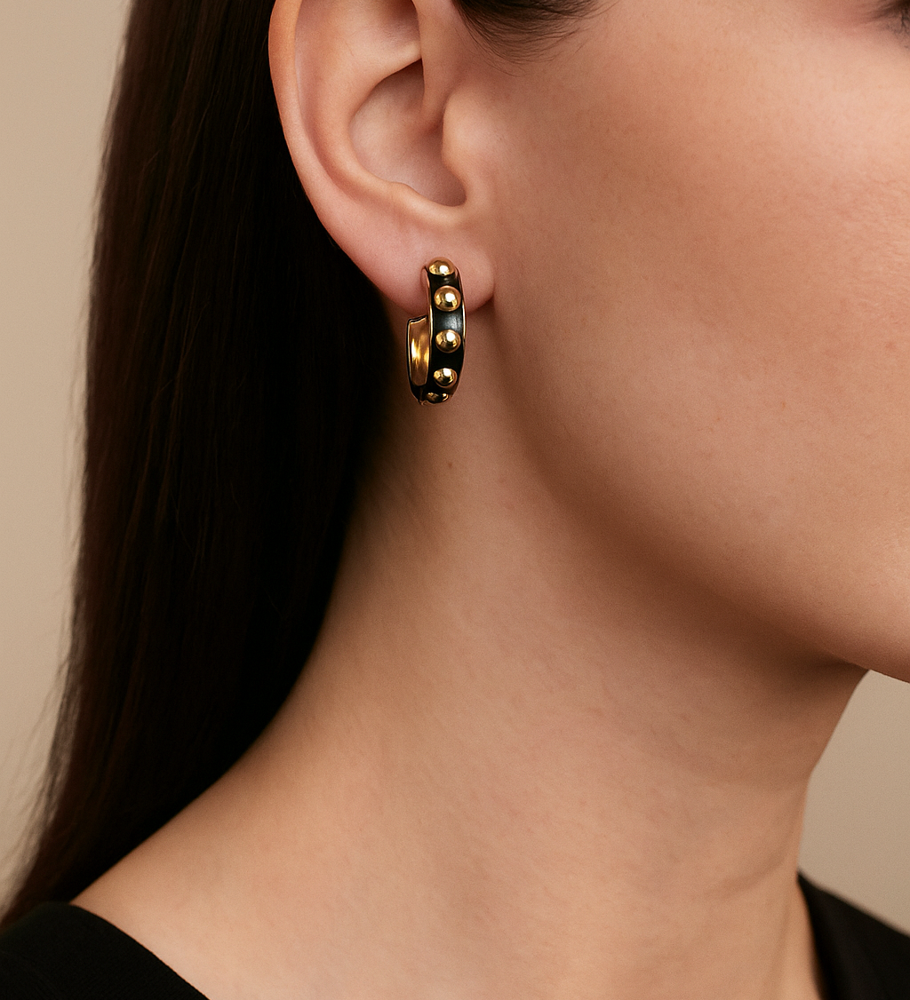 Close-up of a person wearing gold and black beaded hoop earrings with a neutral background