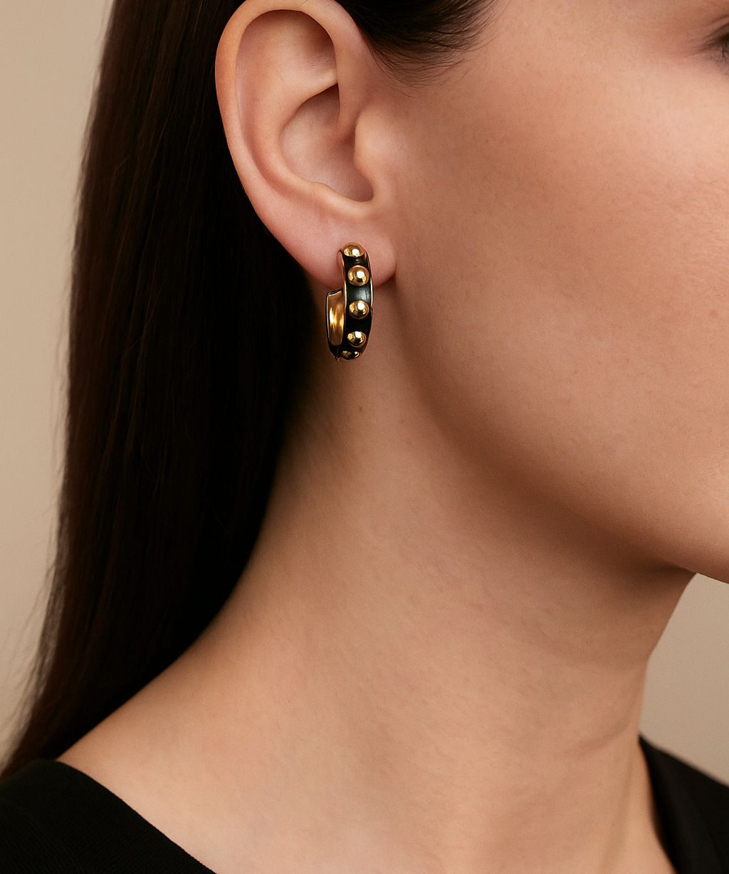 Close-up of a person wearing gold and black beaded hoop earrings with a neutral background