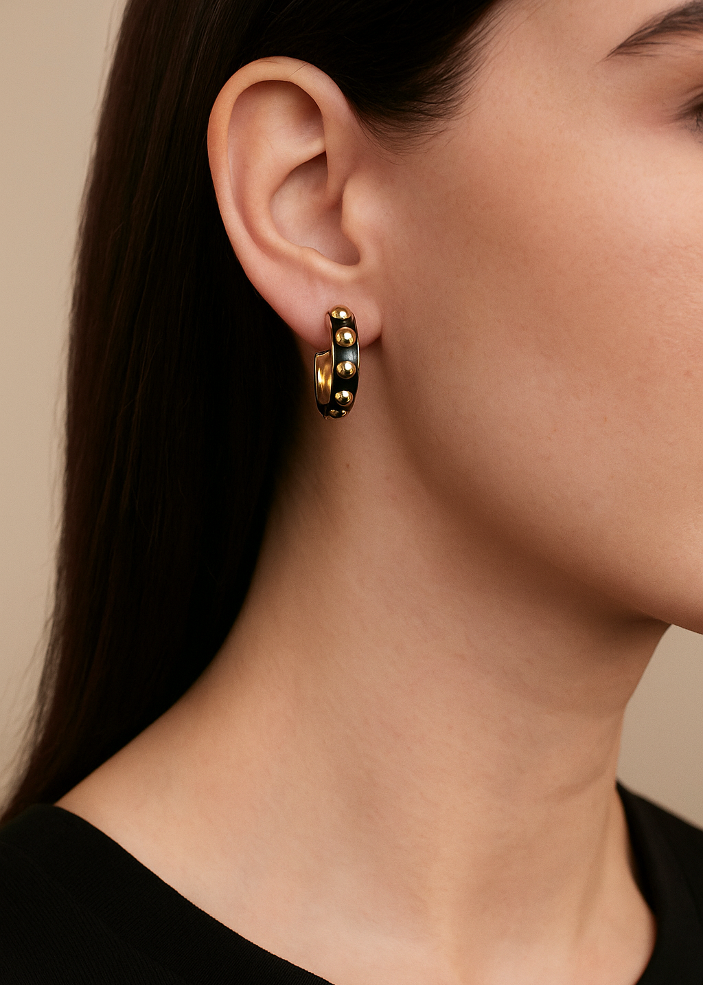 Close-up of a person wearing gold and black beaded hoop earrings with a neutral background
