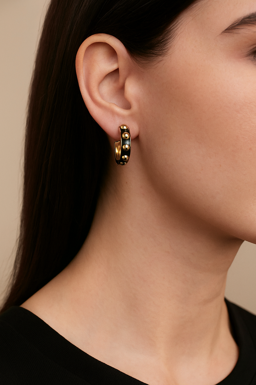 Close-up of a person wearing gold and black beaded hoop earrings with a neutral background