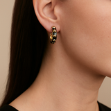 Close-up of a person wearing gold and black beaded hoop earrings with a neutral background