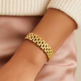 Gold watch band bracelet on a wrist with a neutral background