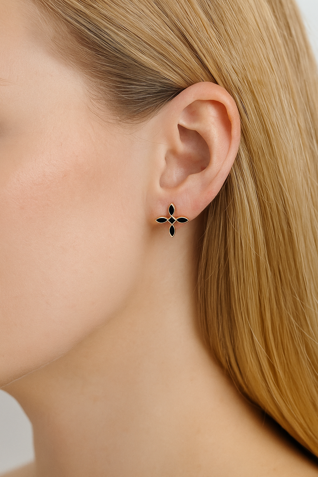 Close-up of a woman with blonde hair wearing a black and gold cross earring.