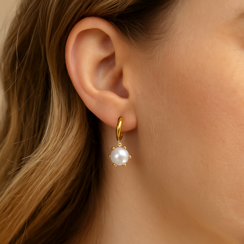 Gold earring with a pearl drop worn by a person with blonde hair.
