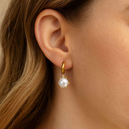 Gold earring with a pearl drop worn by a person with blonde hair.
