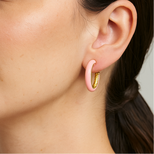 Close-up of a person wearing a pink enamel hoop earring against a neutral background