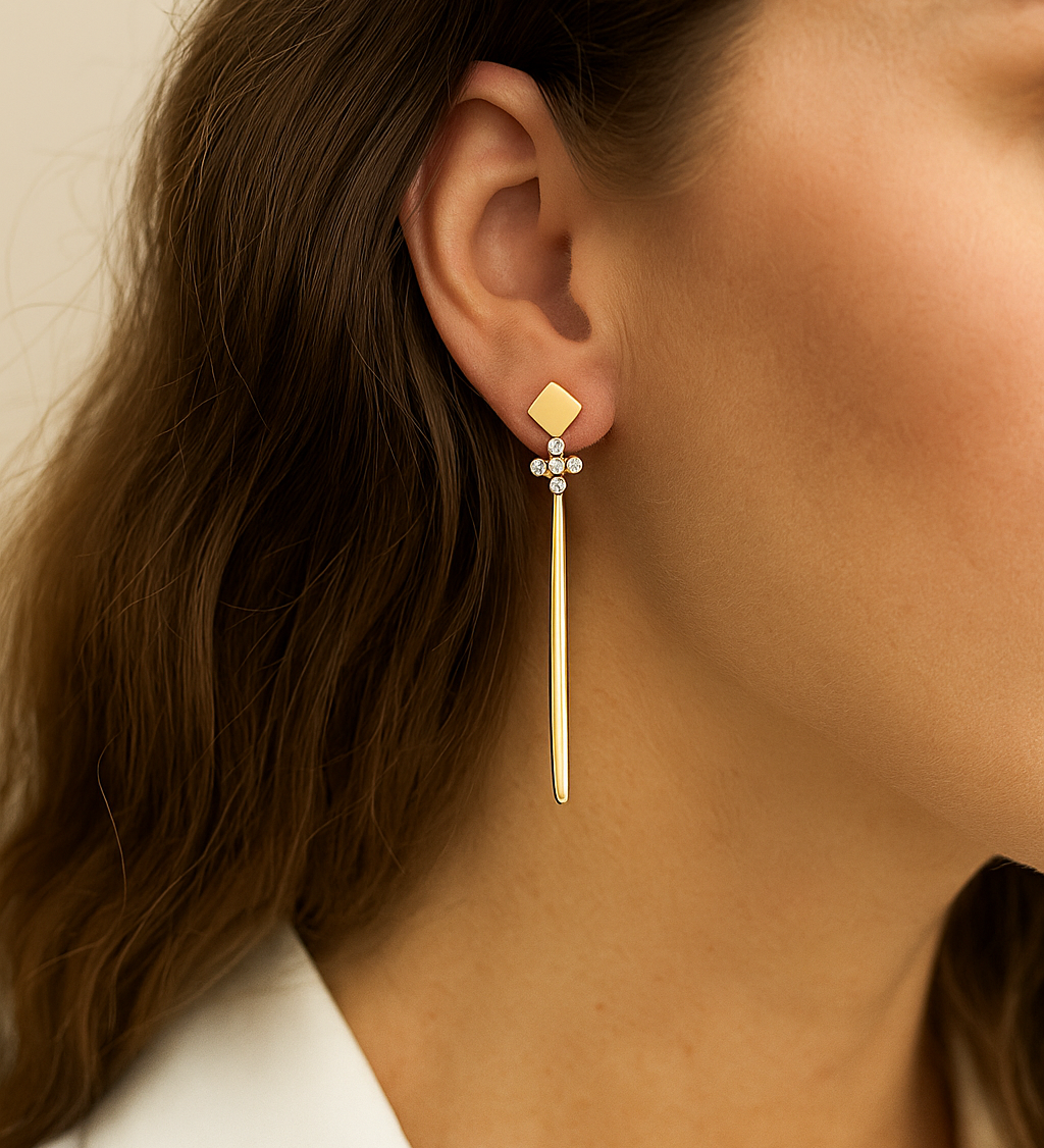 Gold cross earring worn by a person with a neutral background