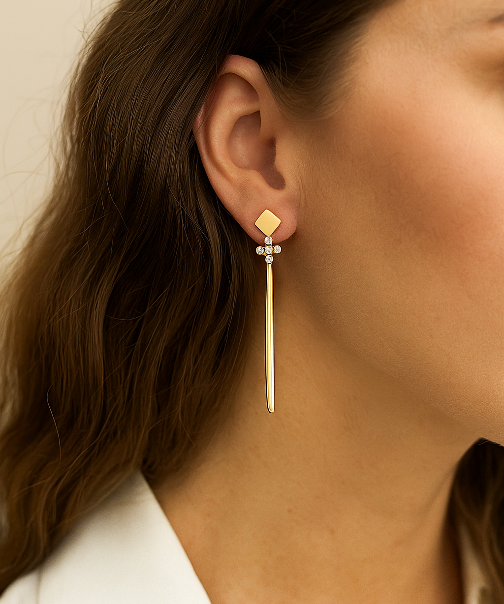 Gold cross earring worn by a person with a neutral background