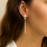 Gold cross earring worn by a person with a neutral background