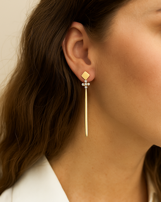 Gold cross earring worn by a person with a neutral background