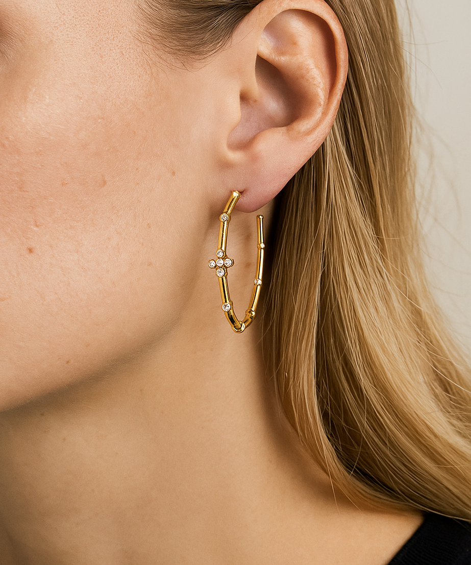 Close-up of a person wearing a gold cross hoop earring with a small gemstone.