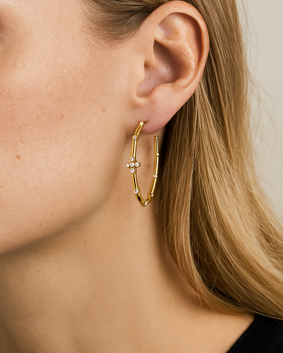 Close-up of a person wearing a gold cross hoop earring with a small gemstone.