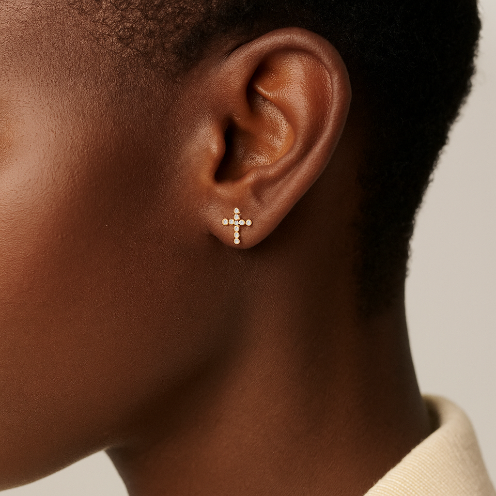 Close-up of an ear wearing a gold cross earring against a neutral background
