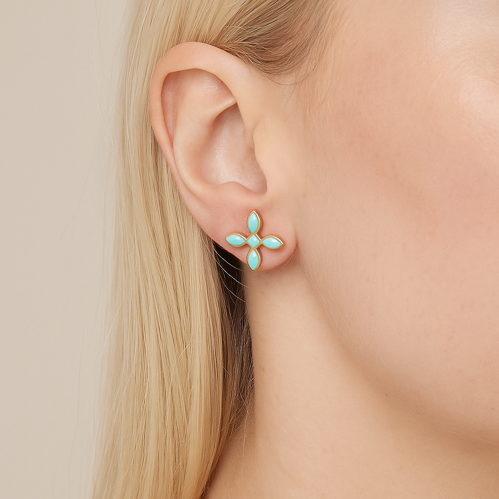 Close-up of a person wearing a mint green cross-shaped earring with a beige background