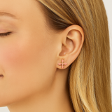 Close-up of a person wearing gold and pink cross earrings with a neutral background