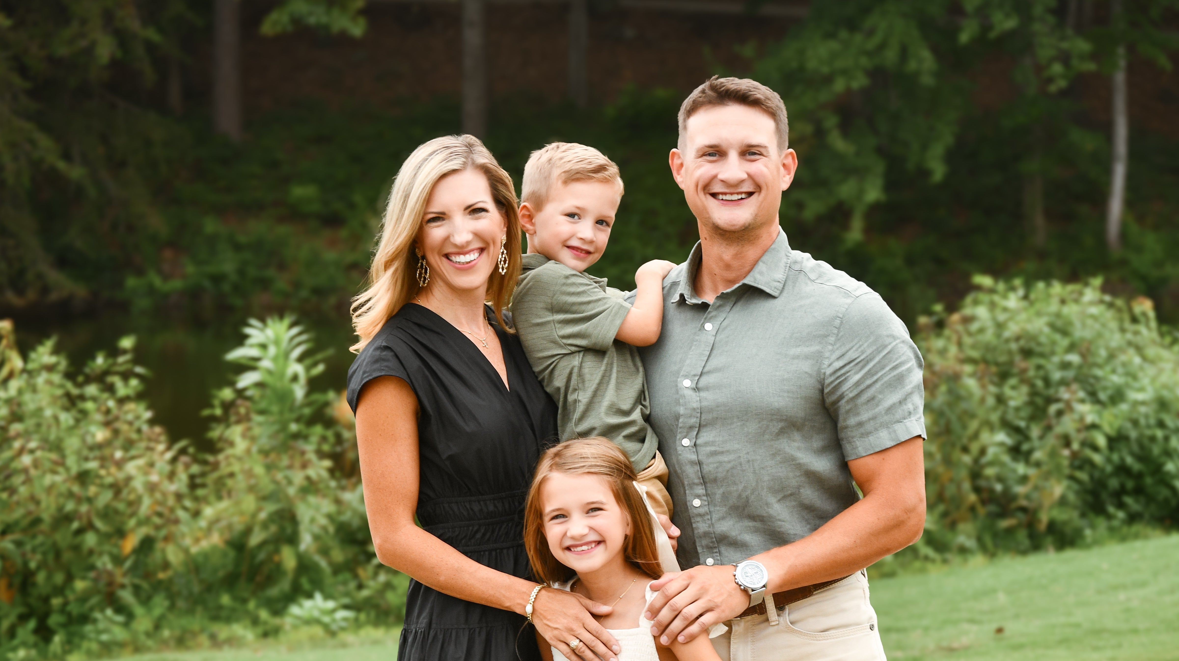 Family of four standing outdoors with greenery in the background