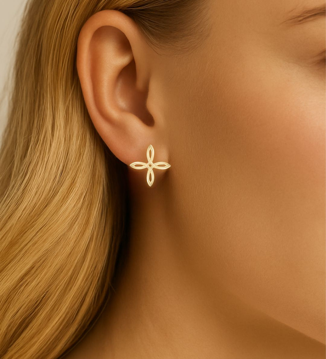 Gold cross earring worn by a person with blonde hair.