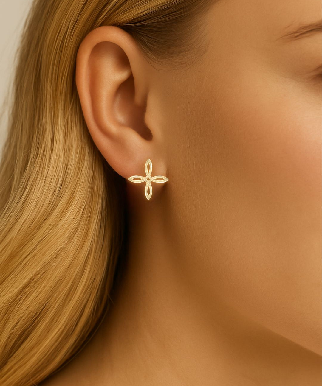 Gold cross earring worn by a person with blonde hair.